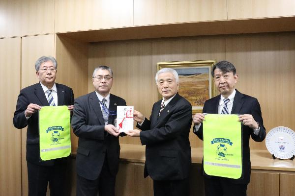 写真：今井会長が近藤教育長に目録を贈呈し、副会長がそれぞれランドセルカバーを持っています。