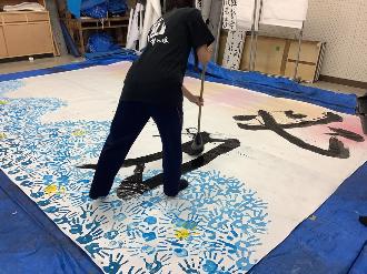 写真：「必勝」の「勝」の3画目を書く高校生の後ろ姿