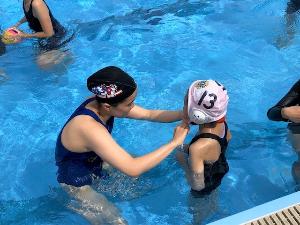 写真：田中選手が女子児童の水球帽子の紐を結んであげています。