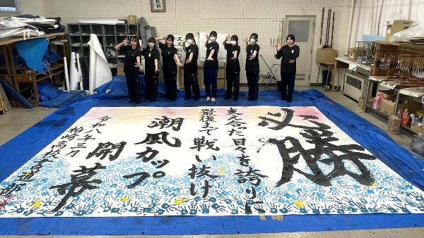 写真：完成した作品と水球のボールを投げるポーズをする書道部の8人の女子部員