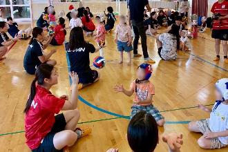 写真：選手と園児がいくつかのグループに分かれ、円になってボールをパスし合っています。園児は水球帽子を被っています