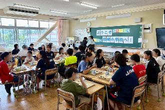 写真：6年生の教室で児童と机を並べて給食を食べました