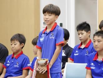 写真：小学生チームキャプテンの笹川選手が抱負を話している様子。優勝カップを持っています
