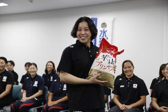 写真：笑顔で米山プリンセス5キロ入りの袋を持つ稲場主将。後ろにいる選手も笑顔です