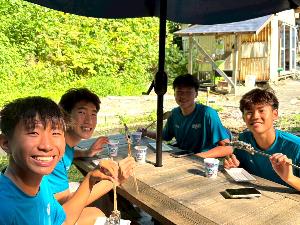 写真：釣ったにじますを食べる選手たち。笑顔です