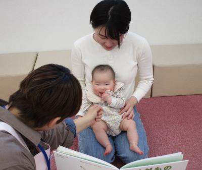 写真：お母さんの膝に抱かれた赤ちゃんに絵本を見せているところ