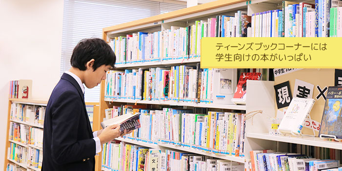 写真：本棚の前で小説をめくる制服姿の男の子