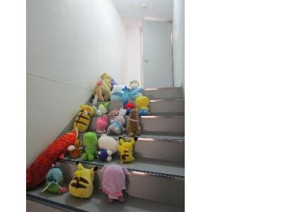 写真：図書館の階段にぬいぐるみが並び、奥のドアに進んでいこうとしています
