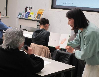 写真：講師が1人の参加者の前で絵本を広げて読み合う様子