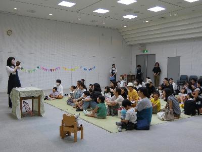 写真：パペットによる「くまさんのおでかけ」を見ている子どもたちと保護者。子どものそばにはお気に入りのぬいぐるみがいます