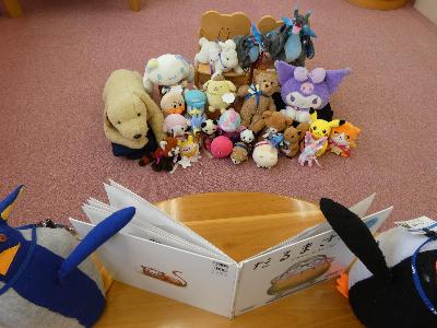 写真：2体のペンギン司書のぬいぐるみが大型絵本の両脇にいます。開いた絵本の前でぬいぐるみたちが読み聞かせしてもらっているかのようです。