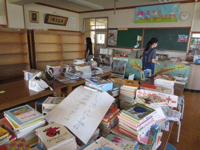 学校にある図書室の本棚から全ての本を出し整理する支援員の写真
