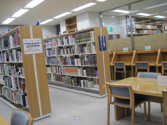 テーブルの奥に、本がずらり並んでいる棚がある参考図書室の写真