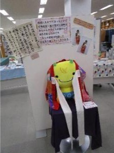 写真：継ぎ寄せの着物の紹介文と黄色い小鬼のぬいぐるみにかけられた継ぎ寄せの着物が展示されています