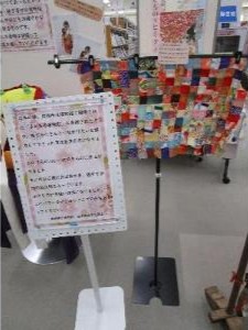 写真：小さな正方形の布を継ぎ寄せてできた生地（製作途中）と、制作過程を説明したパネルがあります