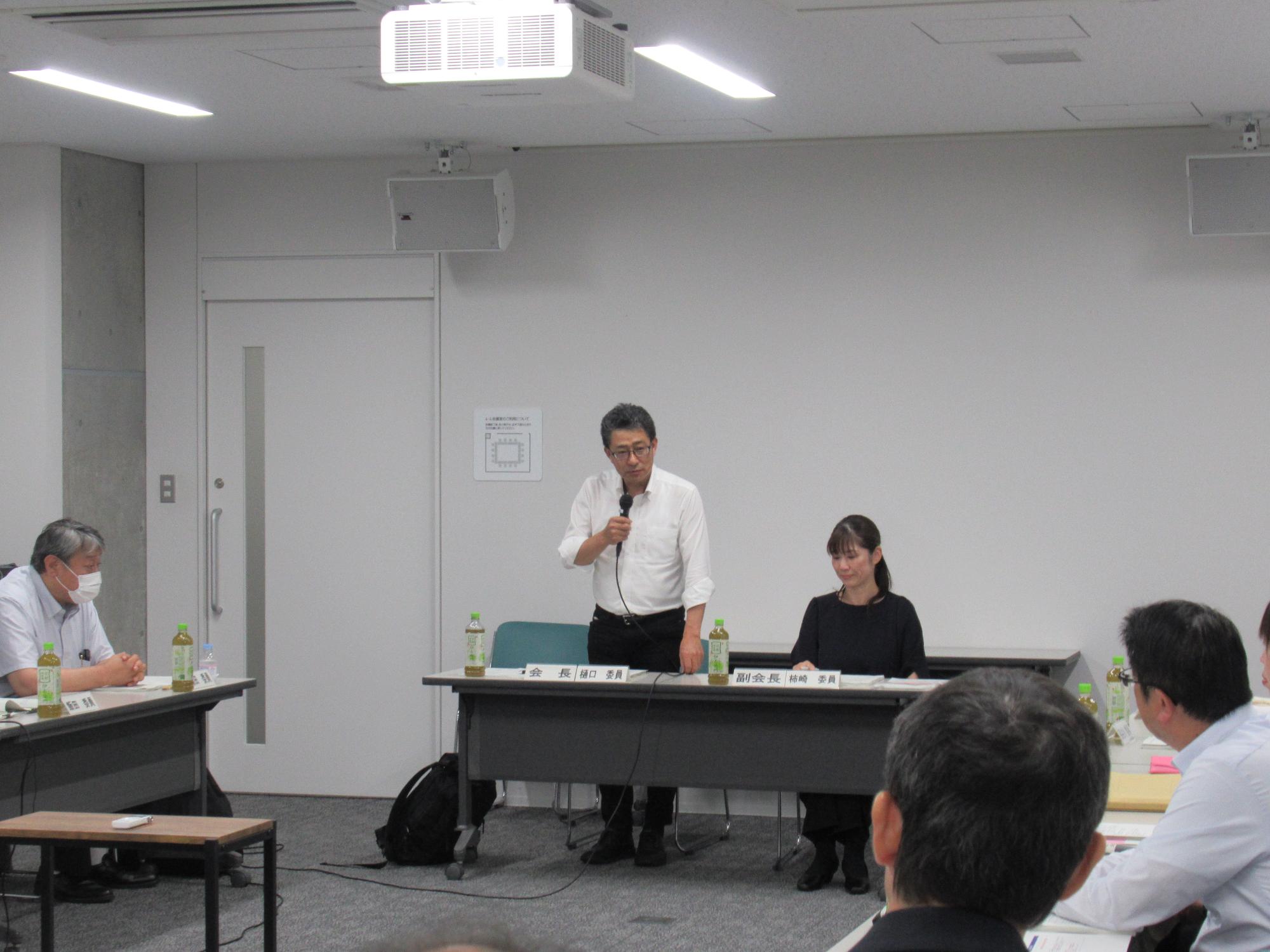 写真：審議会長が起立し、挨拶をしている様子。