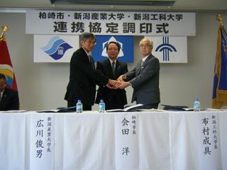 連携協定調印式で市長と二大学学長が握手している写真