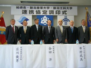 連携協定調印式で参加者7人が調印式の横断看板の前に立っている写真