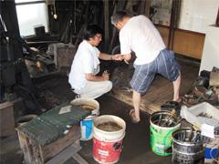 男性2人が鍛冶屋で鍬や用具の調査している写真