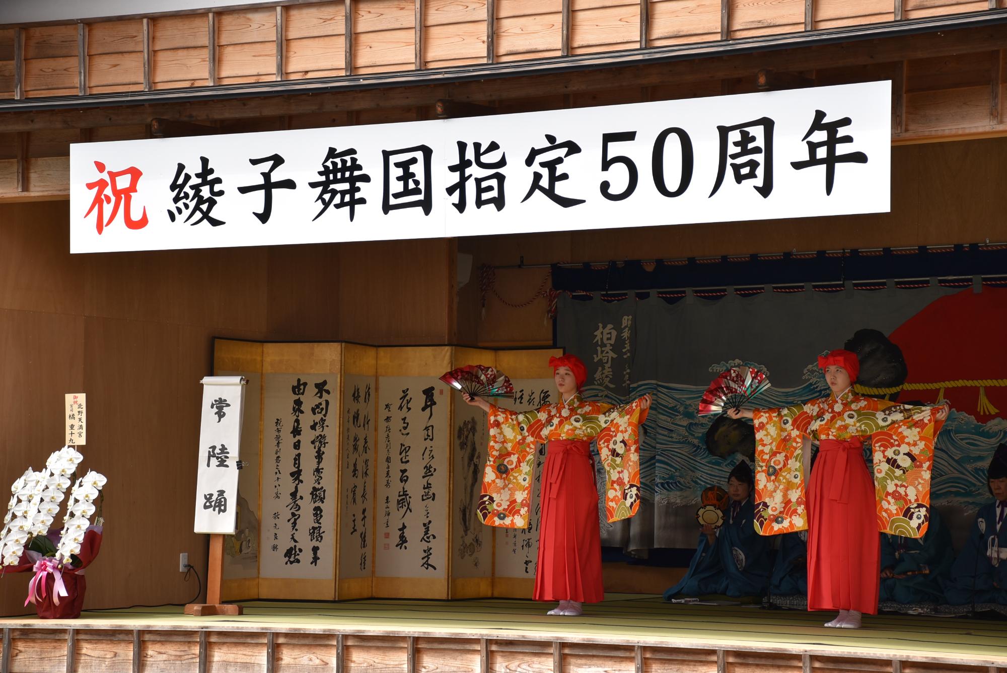 二人の女性が、右手に開いた扇を、左手は着物の袖をつまみ、両手を広げ踊っている写真