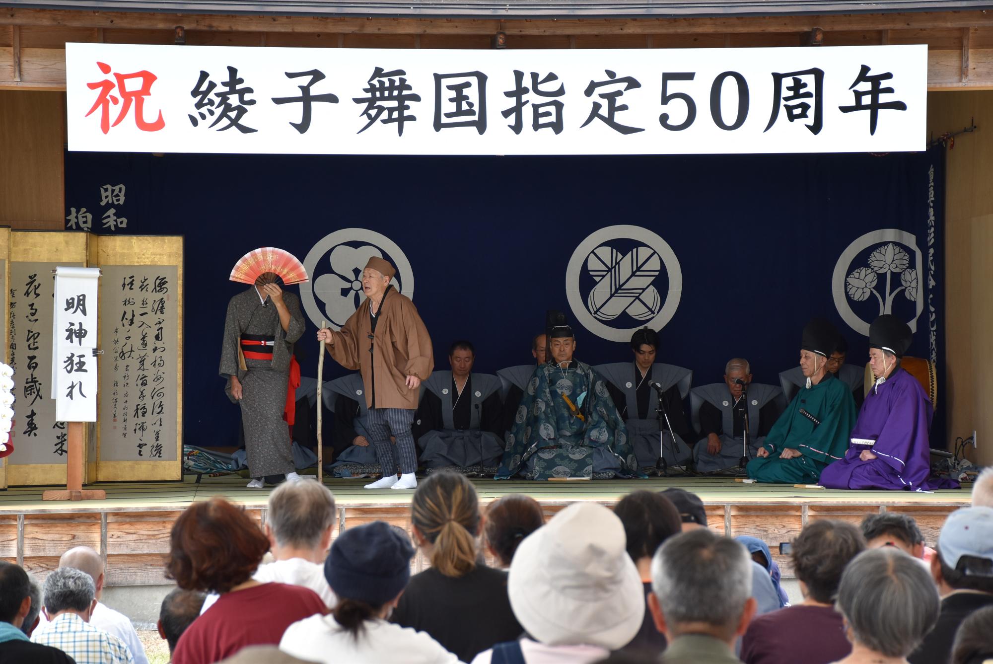 左に夫婦を演じている座頭役の男性と女性役の男性、中央には帝役の男性が座っており、右に社人役である男性が二人座っている写真