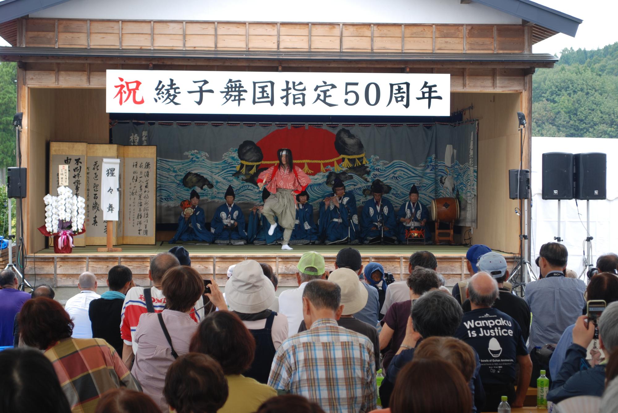 酒に酔った猩々（薄赤の着物に赤いタスキをかけ、長髪に白いハチマキしている）が扇を右手に持ち、左手を腰に当てて舞っている写真