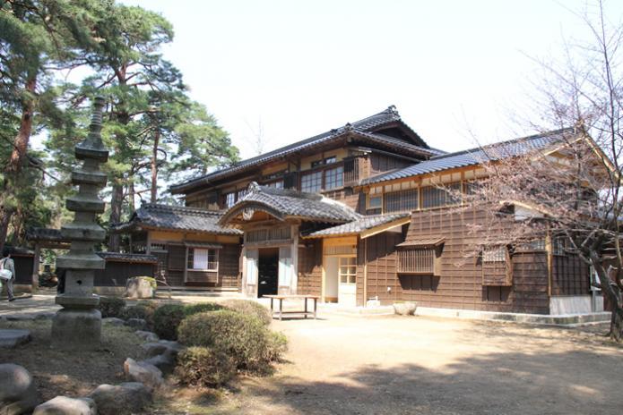 立派な松の木とその手前に石造りの五重の塔ある上質な和風建築とマッチした飯塚邸の庭と主屋の写真