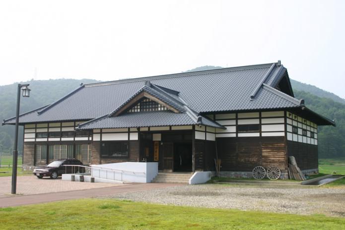 山を背景に田園に囲まれた庄屋風の造りの綾子舞会館の写真