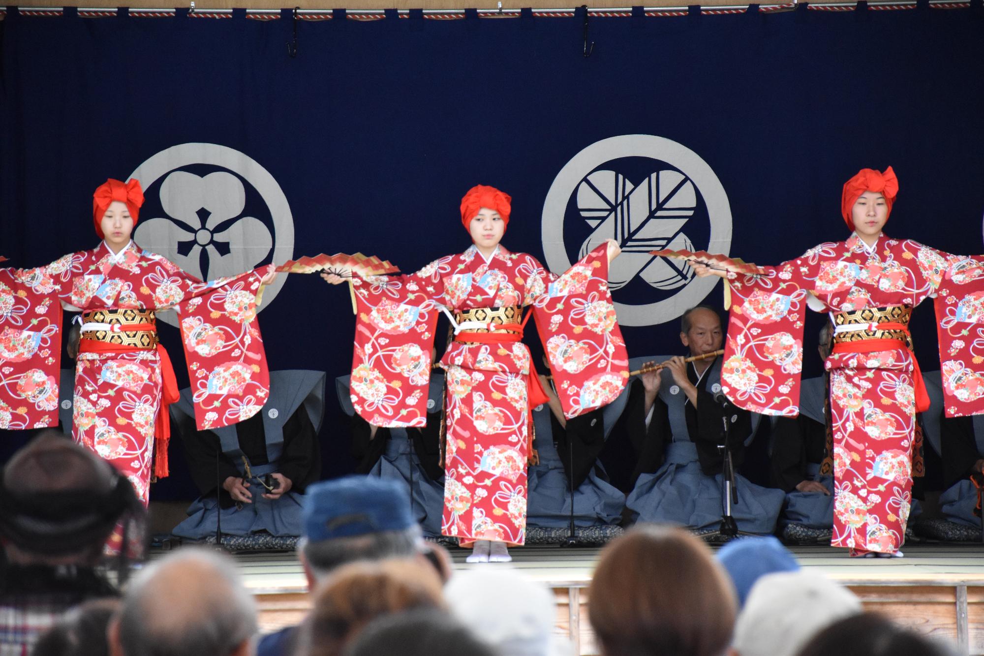 三人の女性が、右手に開いた扇を、左手は着物の袖をつまみ、両手を広げ踊っている写真