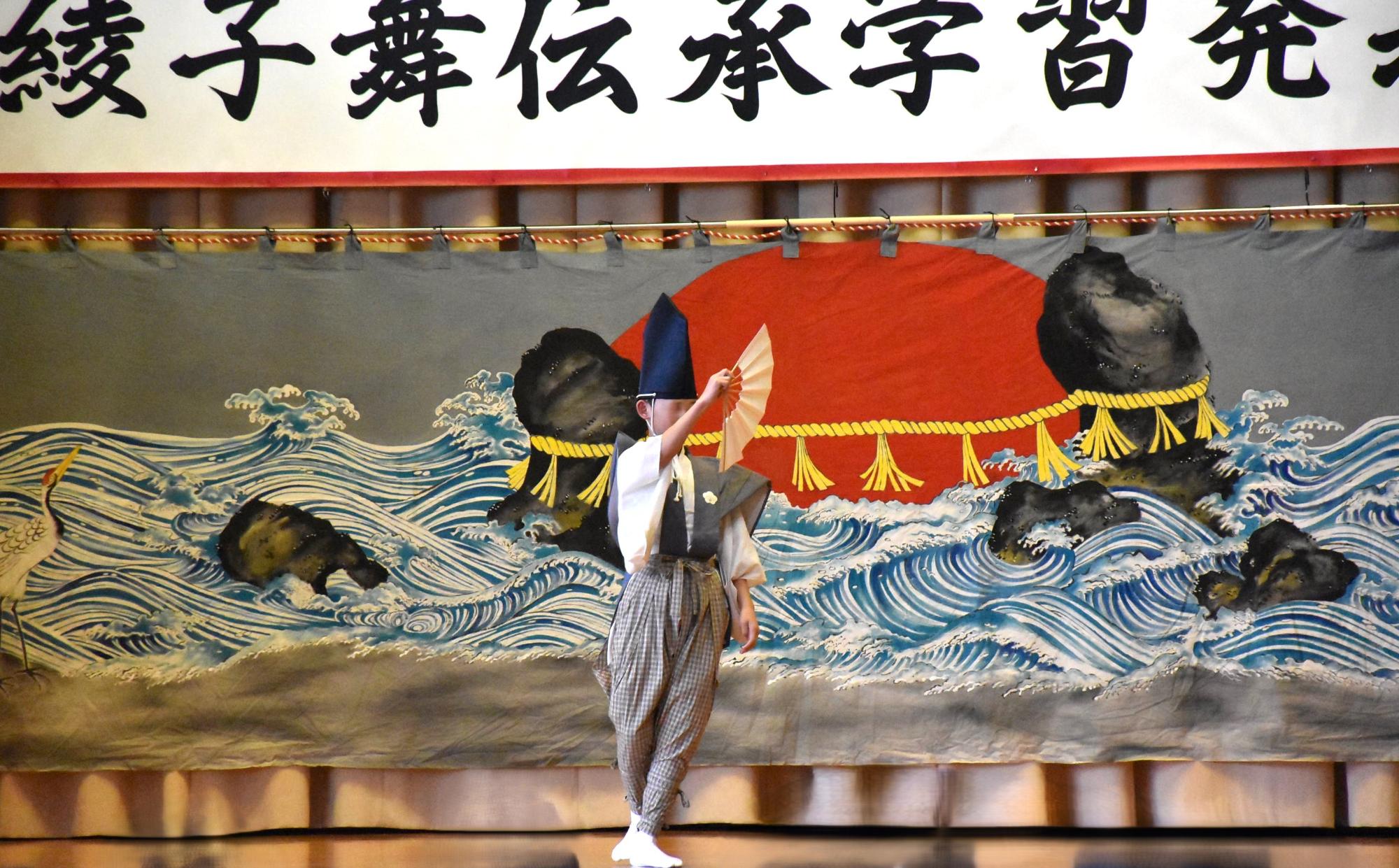 写真：男子生徒が1人で右手に持った扇を自分の前に伸ばし、囃子舞を舞っているところ