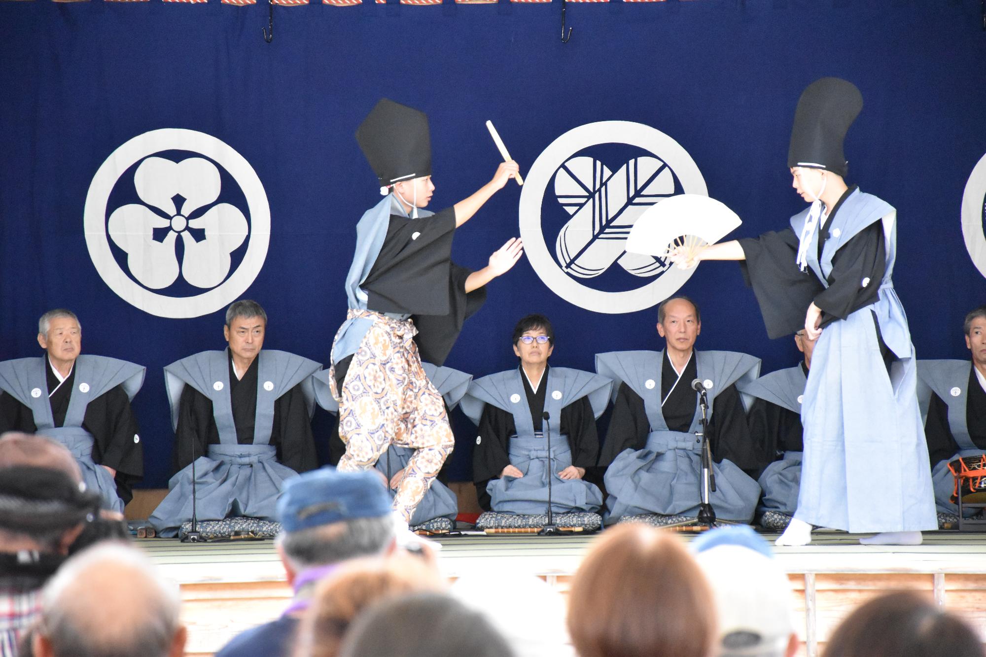 殿様役と冠者役の男性二人が扇を右手に持ち、向かい合って踊りながら会話をしている写真