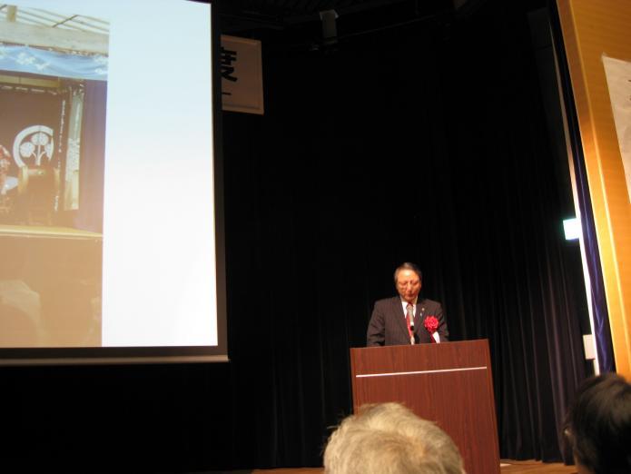 会田市長が会場で大きなスクリーンを使い綾子舞など、柏崎市の紹介をしている写真