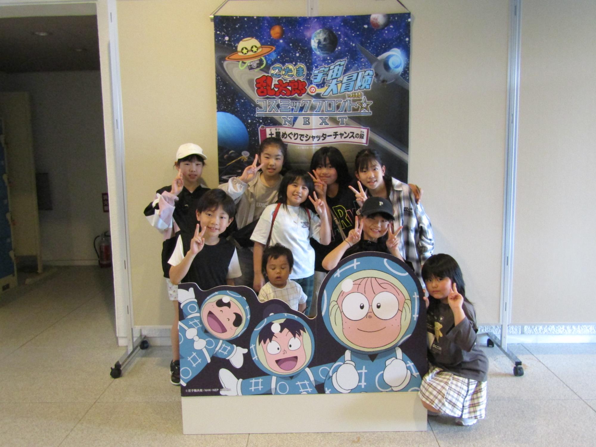 写真：忍者が主人公のアニメ「忍たま乱太郎」のタペストリーの前で写真を撮る9人の子どもたち