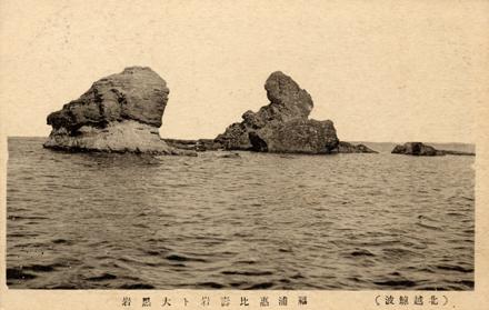 夕日をバックに波間に浮かぶごつごつとした岩肌の笠島の烏帽子岩の写真
