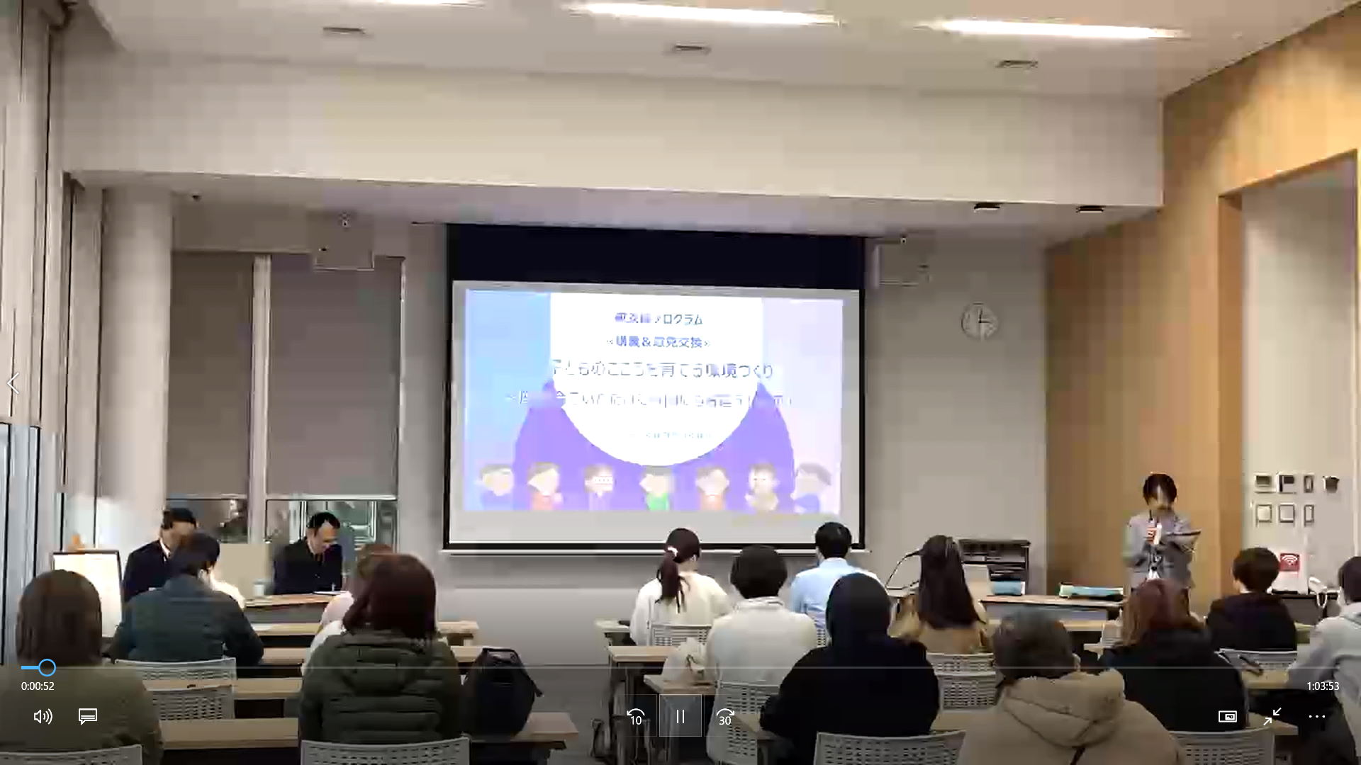 写真：市役所多目的室での講座の様子。前方に資料が映し出され、参加者が話を聞いています。