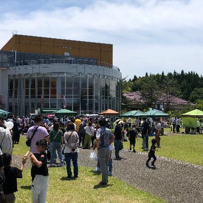 青空の下、西山ふるさと公苑に多くの人があつまり、飲食や買い物をして楽しんでいます