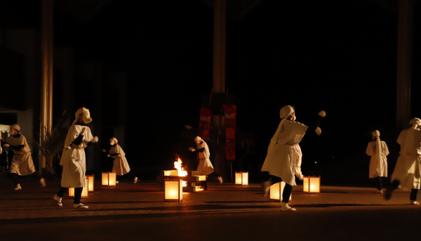 写真：かがり火の周りに行燈を並べ、その外側を狐の装束を着た人たちが踊っているところ