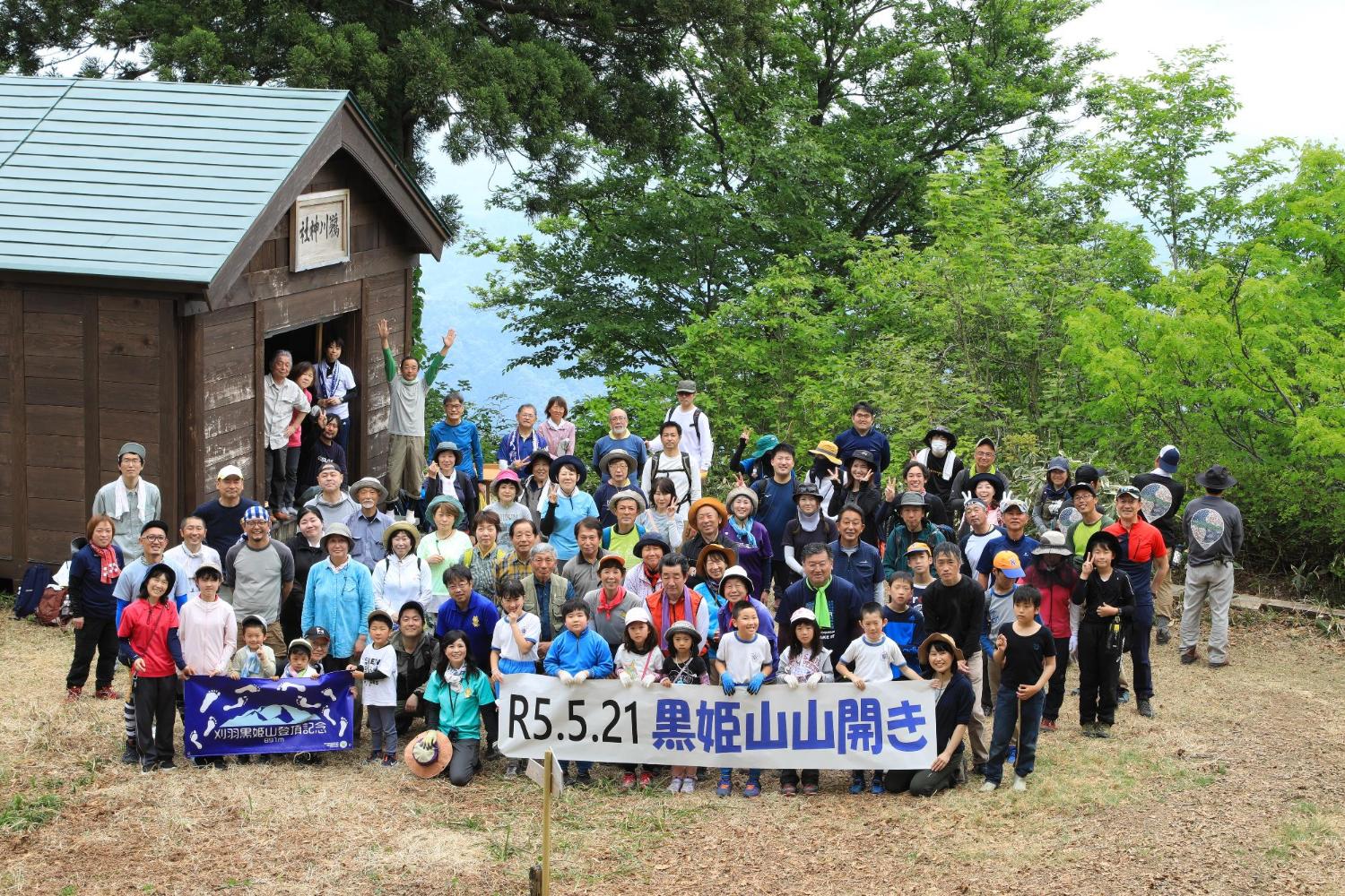 鵜川神社の前で「2023年黒姫山山開き登山記念」の横断幕を前に笑顔で記念撮影している写真