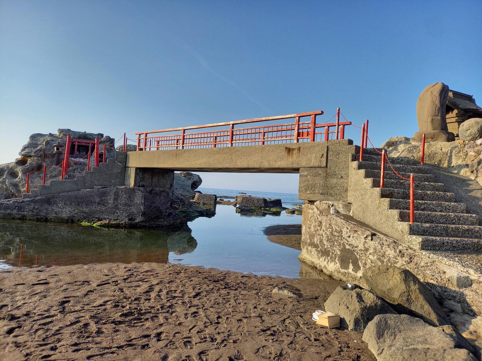 写真：番神海岸。鳥居のある岩場に渡るコンクリートの橋があります。