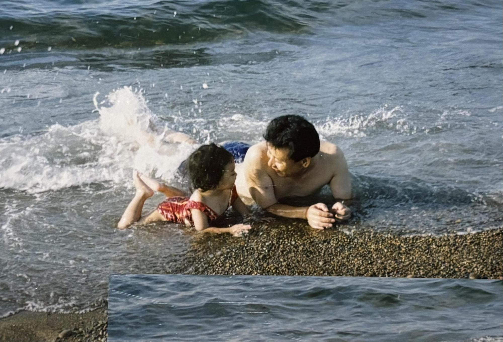写真：番神海岸の波打ち際で寝そべる小さい頃のみゆたそさんとおじいさん