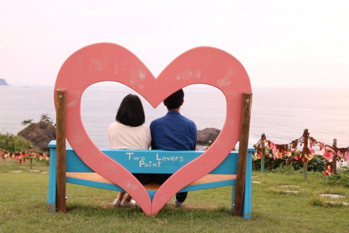 恋人岬に設置されている背もたれにハートがデザインされているビーチベンチにカップルが座っている写真