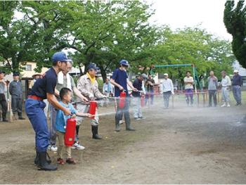 写真：水消火器を使って、子どもたちに使い方を教える地域の消防団員