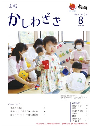 広報かしわざき2022年8月号の表紙：おもちゃのコップを両手に持ち、子育て支援室で遊ぶ女の子。周りには支援室の職員と一緒に遊ぶ親子もいます。