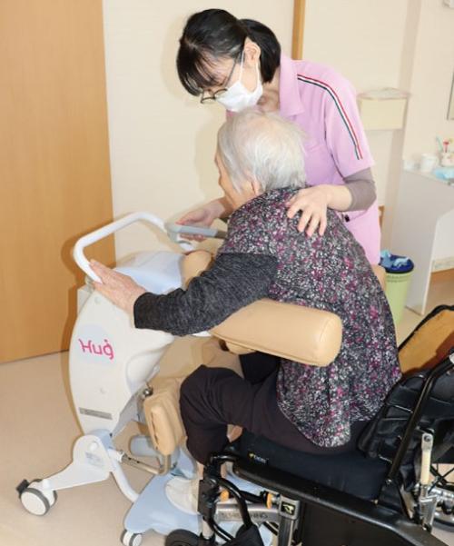 写真：宮川さんが移乗サポートロボットを使って高齢者を車イスに移動させているところ