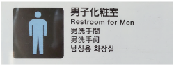 新幹線車両内にある「男子化粧室」のサイン看板。水色をした人型のアイコンと日本語・英語・中国語・韓国語で男子化粧室の文字が書かれています