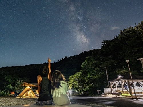 写真：男の子と女の子が夜空を見上げています。夜空には天の川と無数の星が見えます。