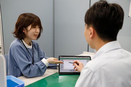 写真：店舗内でタブレットで資料を示しながら接客する尾崎さん