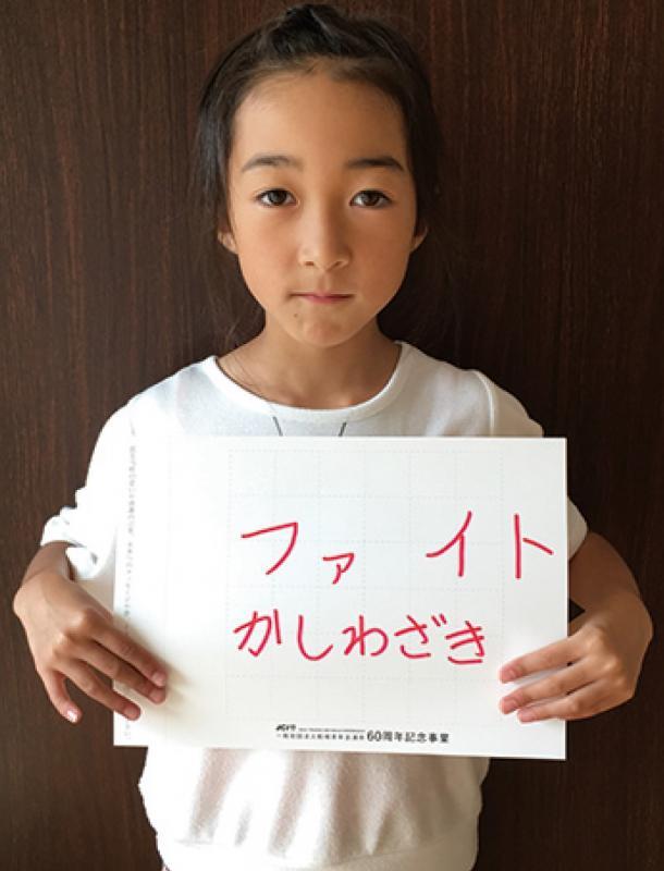 胸の前に「ファイト かしわざき」と書かれた紙を持った田邉さんの写真