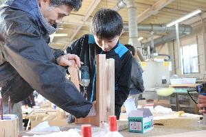 子どもが工具を使ってイスを組み立てています。その作業を大人が手伝っています。