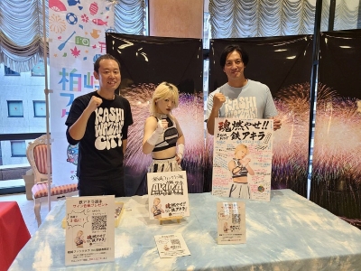 写真：出展ブースの様子。市職員の間に鉄選手が並び、握りこぶしを前に出しポーズをとっています